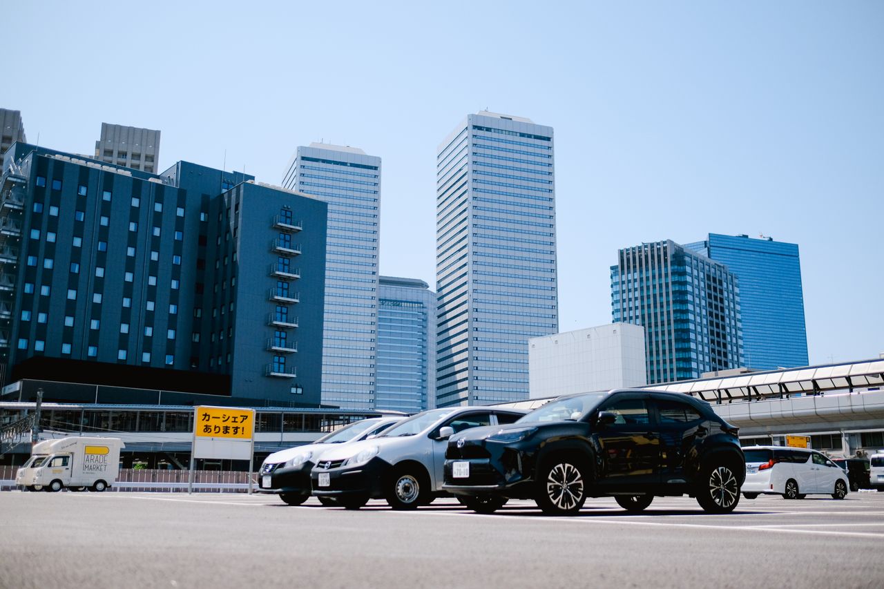 City parking lot with modern buildings and parked cars under a clear sky.